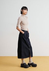 Bež turtleneck pulover, tamnoplava midi suknja s prednjim gumbima, sivi čarape, crne klompe. Glatka tekstura, ležeran dizajn, ravna silueta.