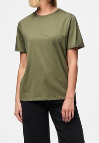 Olivově zelené tričko s krátkým rukávem vyrobené z měkké bavlny. Má klasický kulatý výstřih a mírně zahnulé manžety, s uvolněným střihem.
