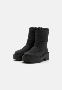 Bottes matelassées noires avec une semelle plateforme haute, texture matelassée, bout arrondi et détail de poignet froncé pour une isolation et une chaleur accrues.