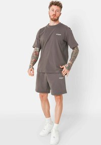 Grijze katoenen t-shirt en bijpassende korte broek set. Losse pasvorm, ronde hals en geborduurd logo op de borst. Witte sneakers maken de outfit compleet.