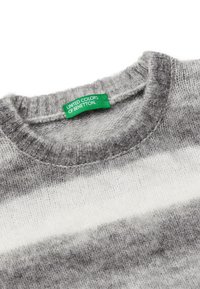 Šedý a bílý pruhovaný svetr s kulatým výstřihem, vyrobený z měkkého materiálu, s zelenou etiketou "United Colors of Benetton".