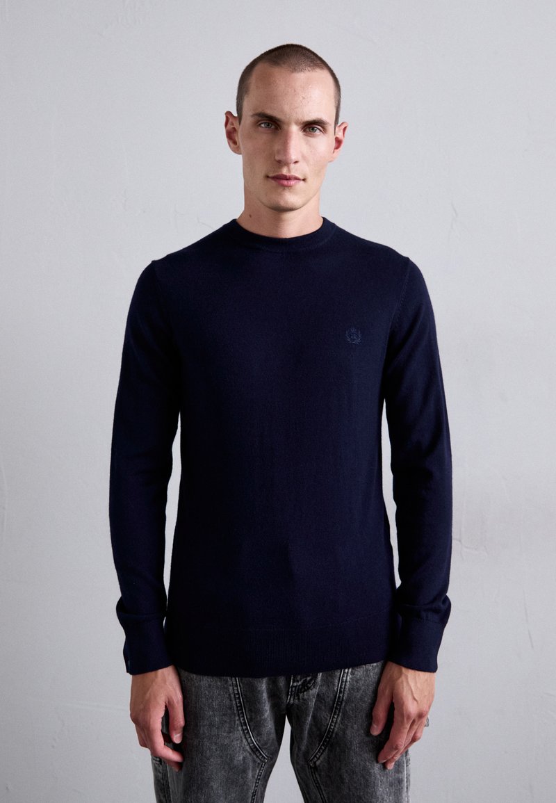 Navy blue knitted sweater with a crew neck and long sleeves, featuring a subtle logo detail on the chest and a fitted design.