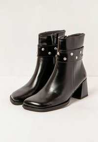 Botas de tobillo de cuero negro con punta cuadrada, tacón medio y correas decorativas con tachuelas alrededor de la parte superior. Cierre de cremallera en el lateral.