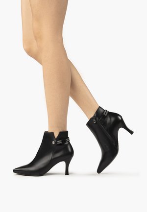 Bottines en cuir noir avec des bouts pointus et des talons hauts, présentant une fermeture éclair d'accent et une sangle décorative avec des embellissements.