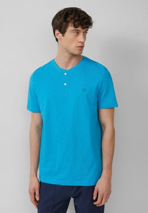 Kurzärmliges, geknöpftes Henley-Hemd in leuchtendem Türkis. Weicher Baumwollstoff mit feiner Textur und kleinem Logo auf der Brust.