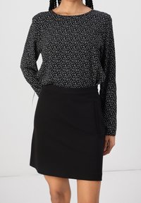 Camiseta negra con lunares blancos y mangas largas, combinada con una falda negra que tiene un bolsillo lateral y una silueta estilizada.