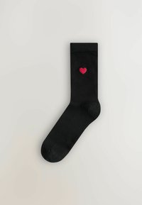 Schwarze Socke mit glatter Textur, versehen mit einem kleinen gestickten roten Herz auf der Oberseite. Klassisches Knöcheldesign.