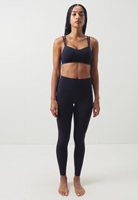 Svart sportsbh med justerbare stropper, kombinert med høyt midjebånd svarte leggings. Begge plaggene har et glatt, elastisk stoff.