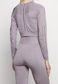 Světle levandulové atletické tričko s dlouhým rukávem a krátkým střihem, s průhledným síťovaným detailem na zádech a žebrovanými manžetami. Hladká, elastická tkanina.