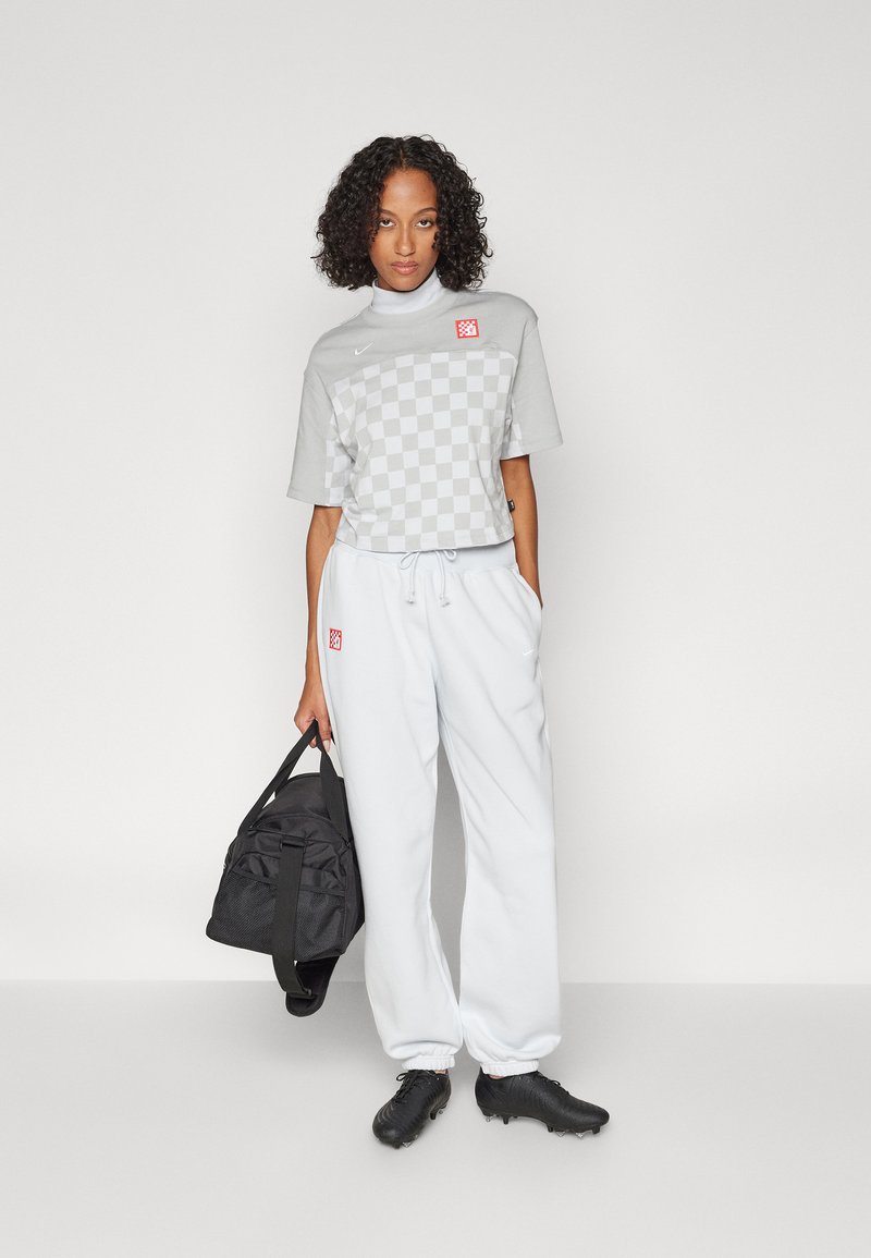 Maglietta corta a quadri grigi, pantaloni della tuta bianchi con coulisse, borsa a tracolla nera e scarpe da ginnastica nere. Design minimalista e estetica sportiva.