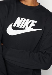 Černá bavlněná mikina s kulatým výstřihem. Na hrudi výrazné bílé logo Nike a žebrované manžety.