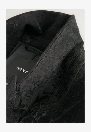 Mustriline tekstuuriga must kangas, millel on lillemuster, pointeeritud kraega ja hoolduslabel kinnitatud rõiva sisse.