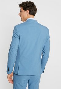 Chaqueta de traje azul claro con un corte entallado, dos respiraderos traseros y botones negros en los puños. Tejido suave con una textura sutil.