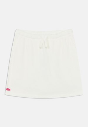 Jupe en coton blanc avec une taille élastique et un cordon de serrage, présentant un petit logo rose sur le côté inférieur gauche. Texture lisse, design décontracté.