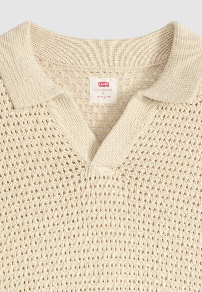Polo beige tejido de punto abierto con cuello acanalado y etiqueta Levi's que indica talla mediana y corte relajado.