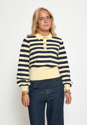 Gestreiftes Pullover-Sweatshirt in Gelb und Marineblau mit Kragen, drei Knöpfen und Puffärmeln. Getragen mit dunklen Jeans.