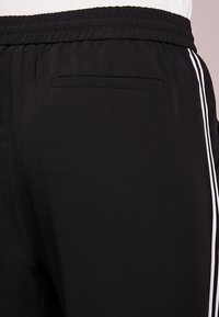 Svarta sportbyxor med elastisk midja, ett bakfickor och två vita vertikala ränder på sidsömmen.