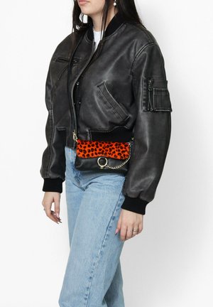 Giubbotto bomber in pelle nera con design corto, dotato di polsini a coste e una tasca. Abbinato a jeans azzurri a vita alta e una piccola borsa con stampa leopardata arancione.