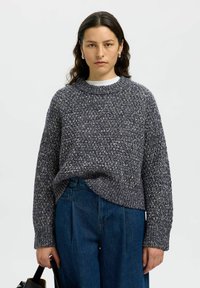 Sweter dzianinowy w ciemnoszarym kolorze z teksturowanym wzorem. Posiada okrągły dekolt i luźny krój, zestawiony z niebieskimi spodniami typu wide-leg. Prosty styl.