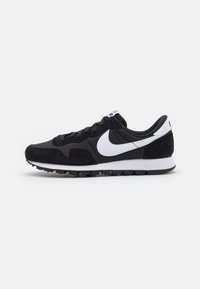 Mustat urheilukengät, joissa on nahkaa ja tekstiilimateriaaleja, valkoisella Nike Swoosh -logolla, nauhakiinnitys ja teksturoitu kumipohja.
