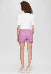 Witte top met korte mouwen, gecombineerd met roze denim shorts. De shorts hebben opgerolde uiteinden en achterzakken, aangevuld met lichtgekleurde sneakers.