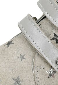 Graue Wildlederschuhe mit silbernen Sternmustern, die über zwei graue Riemen und einen silbernen Druckknopf verfügen. Glatte Textur und genähte Details.
