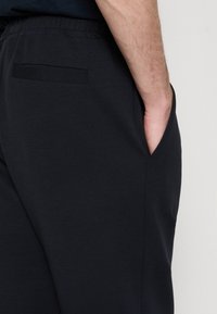 Mörkgrå bomullsbyxor med elastisk midja, med sidofickor och en bakficka, i en mjuk och bekväm textur.