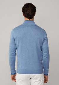 Svijetloplava pletena majica s ovratnikom, dugim rukavima i rebrastim manžetama i rubom. Mekana tekstura, prilagođeni dizajn i minimalno detaljiranje.