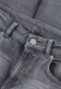 Jeans de denim gris con un diseño clásico de cinco bolsillos, que presentan un cierre de botón de metal, detalles de costura y una sutil textura deslavada.