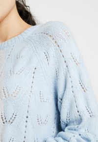 Maglione a maglia azzurro chiaro con un delicato motivo a pizzo ed un collo e polsini a coste. Tessuto morbido e testurizzato, vestibilità leggermente oversize.