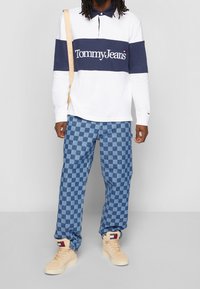 Bílá bavlněná polo košile s dlouhým rukávem a námořnickým horizontálním pruhem a logem "Tommy Jeans"; modré a světle modré kostkované džíny; béžové tenisky.