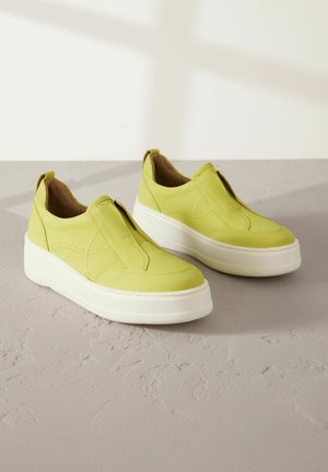 Svijetlozelene slip-on tenisice s glatkom kožnom gornjom površinom, bijelim platformama i suptilnim detaljima šivanja. Sintetička podloga.