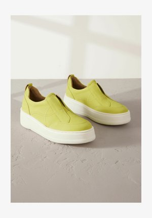 Lime roheline libisev tossud, millel on sile nahk pealmine osa, valge platvormi tallaga ja peened õmblused. Sünteetiline taust.