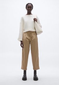 Hosszú ujjú krémszínű pulóver, bézs magas derekú nadrág és fekete platform csizma. A modell fehér válltáskát tart, lazított fazont mutatva.