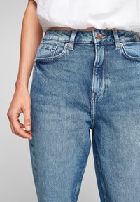 Light blue denim jeans featuring a high waist, five pockets, and button closure. Slightly faded texture with visible stitching details.