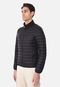 Giacca a puffo nera con zip frontale, colletto alto e motivo a righe orizzontali; include tasche laterali e un design aderente.