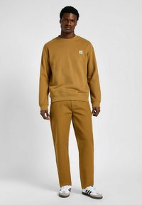 Brązowy bawełniany sweatshirt z ściągaczami, w połączeniu z dopasowanymi spodniami. Sneakersy z białymi, czarnymi i szarymi akcentami. Prosty detal logo.