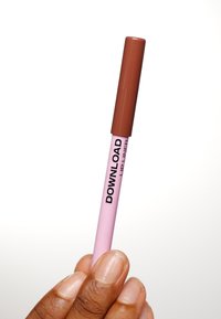 Brun läppennapenn med en rosa kropp, märkt "LADDNING NEDANFÖR," hålls i en hand. Toppen är blank och designen är slank och cylindrisk.