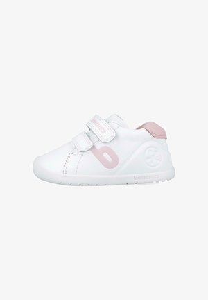 Zapatilla blanca con acentos en rosa, que cuenta con dos correas de Velcro, una puntera redondeada y un logo en el lateral. Fabricada con material sintético suave.