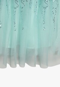 Tissu en tulle bleu clair avec des sequins argentés en motifs de tourbillon verticaux, superposé sur un matériau bleu solide au bord inférieur.