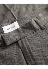 Grijs geruite stof met een subtiele textuur en een elastische tailleband. Bevat een wit label met de tekst "LES DEUX." Zichtbare stikseldetails.