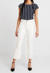 Blusa a righe navy con maniche corte abbinata a pantaloni bianchi a vita alta e a tre quarti con cucitura centrale, e décolleté neri a punta.
