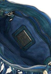 Interno di una borsa in pelle blu con chiusura a zip, caratterizzato da una fodera in tessuto texture e un'etichetta del marchio in rilievo.