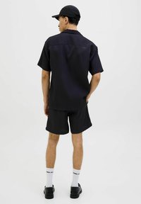 Sort ribbet kortærmet skjorte og matchende shorts, båret med en sort kasket, hvide sokker og sorte sko. Enkel, struktureret design.