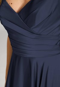 Marineblaues Kleid mit V-Ausschnitt und gerafftem Oberteil. Hergestellt aus glattem Stoff, verfügt es über Falten für Textur und ein fließendes Rockdesign.