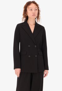 Blazer doppiopetto nero con rever a sodini, caratterizzato da due tasche frontali e dettagli in bottone. Tessuto liscio e strutturato, vestibilità sartoriale.