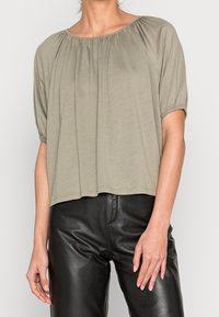 Top corto a maniche corte di colore verde oliva con scollatura arrotondata, dettagli arricciati sulle spalle e vestibilità relaxed, abbinato a pantaloni in pelle nera.