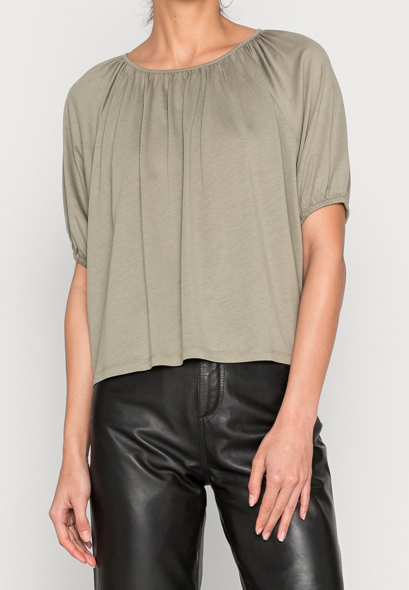 Top corto a maniche corte di colore verde oliva con scollatura arrotondata, dettagli arricciati sulle spalle e vestibilità relaxed, abbinato a pantaloni in pelle nera.