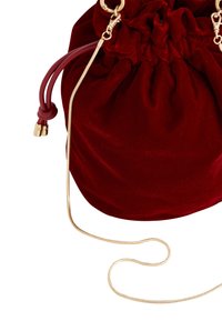 Red velvet drawstring bag with gold chain strap, featuring a gathered top and contrasting leather accents. Smooth texture and shiny hardware.