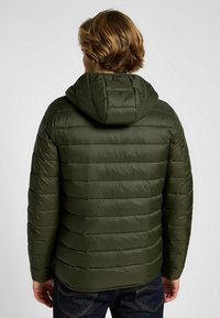 Olivgrön vadderad jacka med huva, med horisontell sömnad, slät yta och elastiska ärmslut. Bakifrån visas en sömlös design.